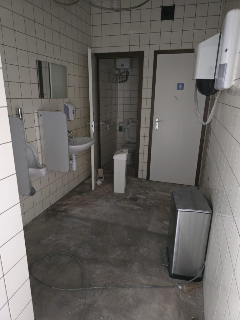 Voor de renovatie: sanitaire ruimte met verouderde tegels en voegen, moeilijk te onderhouden en minder hygiënisch.