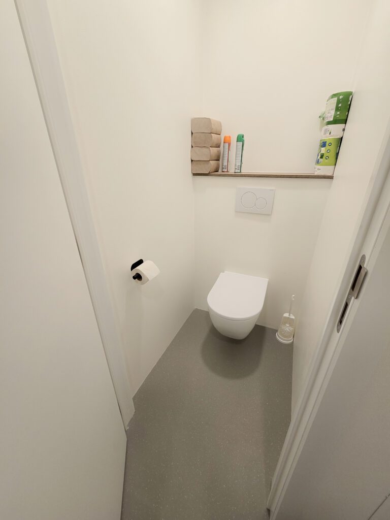 Naadloze afwerking in sanitaire ruimte: PU gietvloer in warme tint met flakes en witte wanden.