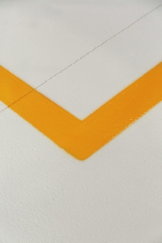 Detail van de PU-toplaag met oranje veiligheidsmarkering voor zoneafbakening in industriële toonzaal